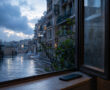 Ventana abierta tras la lluvia, calle mojada y un móvil boca abajo sobre el alféizar.